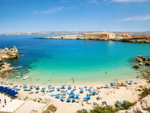 Blue umbrella on tropical beach with white sand, turquoise sea water and blue sky at deserted island in Malta, Paradise bay.